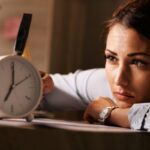 displeased businesswoman hitting alarm clock with hammer office